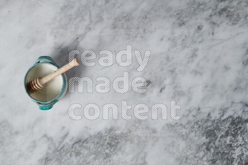 Multicolored pottery bowl with wooden honey dipper in it on grey marble background