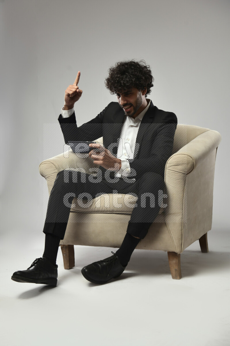 A man wearing formal sitting on a chair gaming on the phone on white background