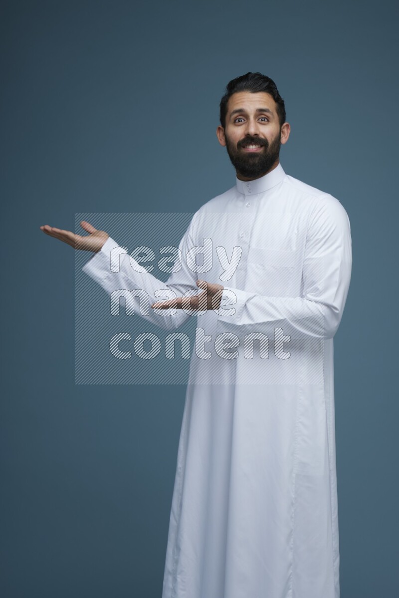 A man pointing in a blue background wearing Saudi Thob