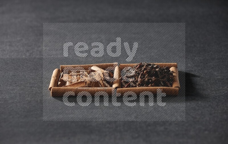 مربعان من أعواد القرفة ممتلئان بالقرنفل وقطع القرفة علي خلفية سوداء