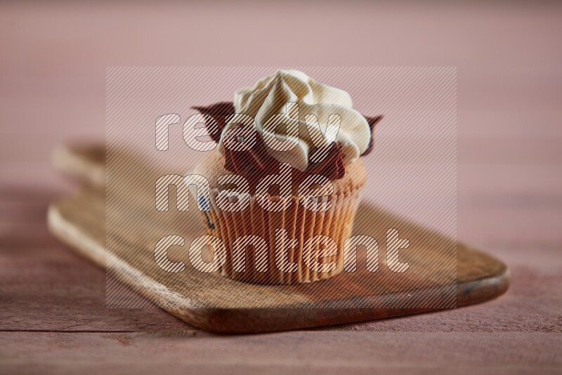 Vanilla cupcake topped with cream on a wooden board