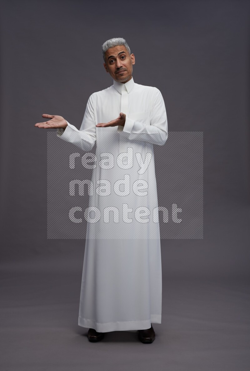 Saudi man wearing thob standing interacting with the camera on gray background