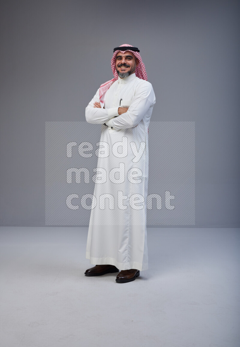 Saudi man Wearing Thob and red Shomag standing with crossed arms on Gray background