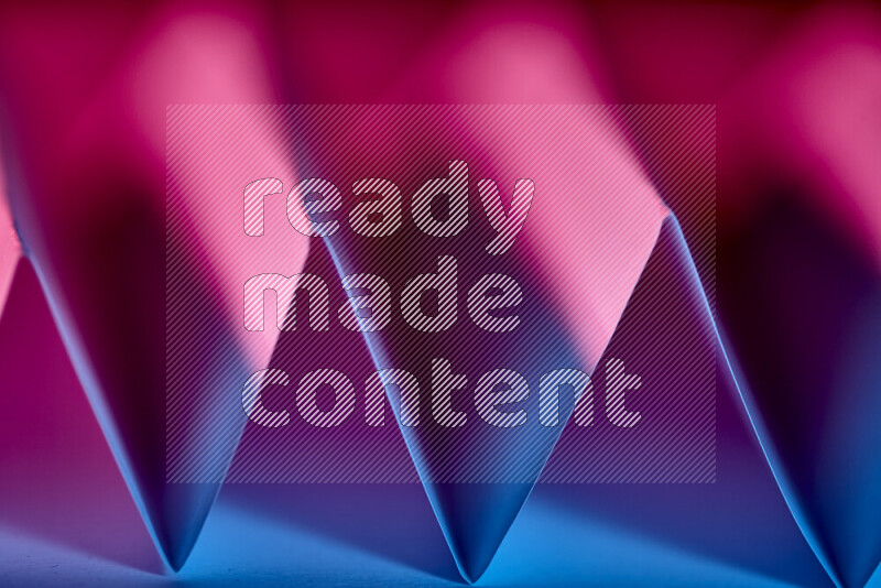 A close-up abstract image showing sharp geometric paper folds in blue and pink gradients