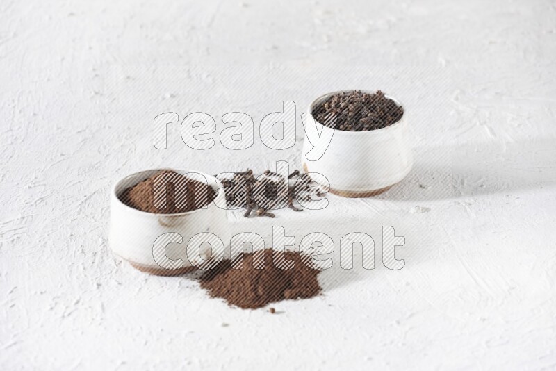 2 Beige ceramic bowls, one full of cloves and the other full of powder on textured white flooring