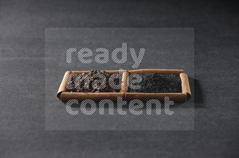 مربعان من أعواد القرفة ممتلئان بحبة البركة السوداء والقرنفل علي خلفية سوداء