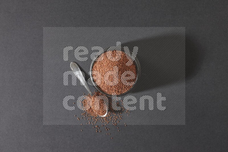 وعاء فخاري أسود ممتلئ ببذور حب الرشاد مع ملعقة معدنية ممتلئة بالبذور على أرضية سوداء