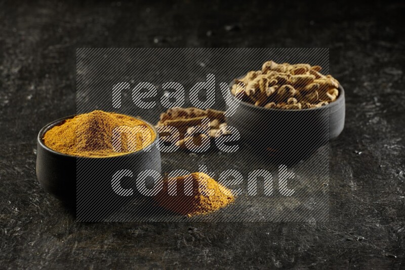 وعاءان من الفخار باللون الأسود، أحدهما ممتلئ ببودرة الكركم والآخر ممتلئ بأصابع كاملة من الكركم المجفف على خلفية سوداء