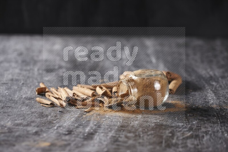 Herbal glass jar full cinnamon powder flipped and a metal spoon full of powder surrounded by cinnamon sticks on textured black background in different angles