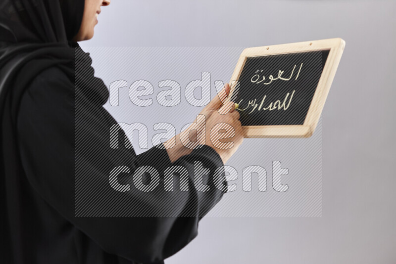 A woman in abaya holding books and a board in different positions (back to school)