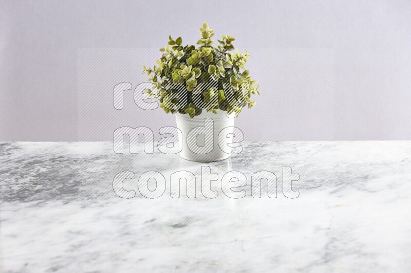 Green artificial plant in white pot on light grey marble background