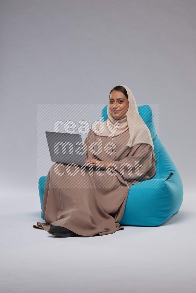 A Saudi woman sitting on a blue beanbag and working on laptop