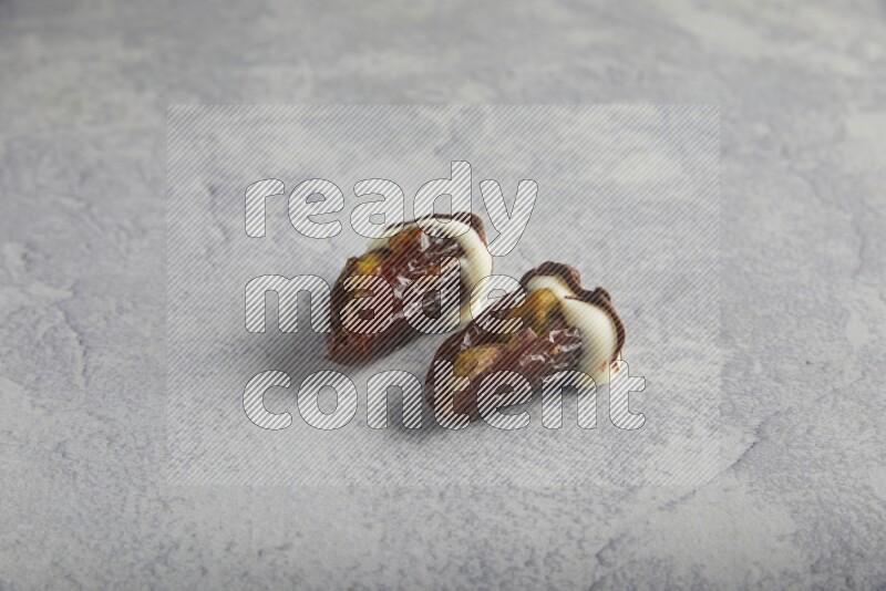 two pistachio stuffed dates covered with white chocolate with dark chocolate drizzle on a light grey background