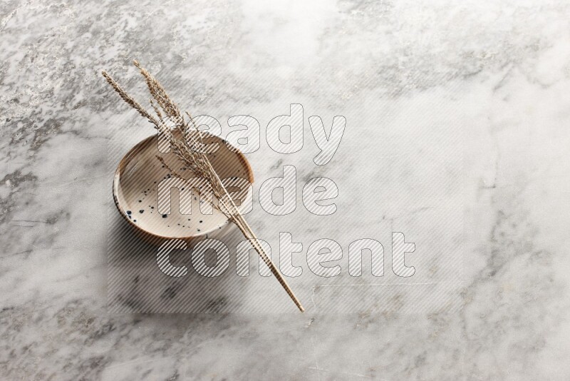 Wheat stalks on multicolored pottery bowl on grey marble background