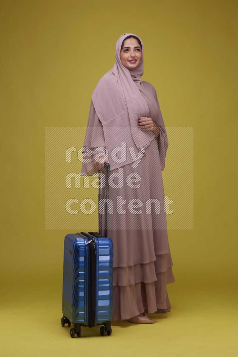 A woman With suit Case on a Yellow Background wearing Brown Abaya with Hijab