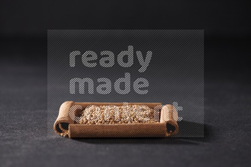 أربعة من أعواد القرفة مكونة شكل مربع بداخلها حبوب الخردل علي خلفية سوداء