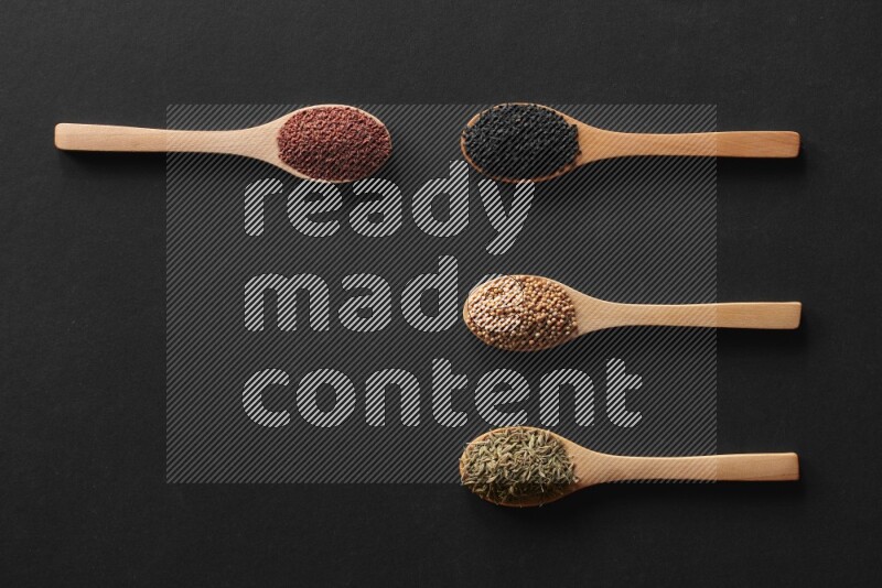 wooden spoons filled with white peppers, mustard seeds, black seeds, garden cress, cumin and flax on black flooring
