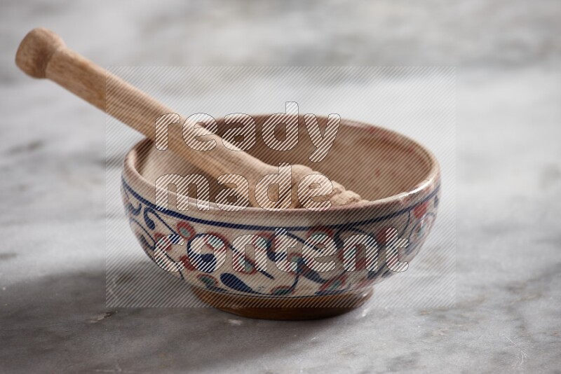 Decorative pottery bowl with wooden honey dipper in it on grey marble background