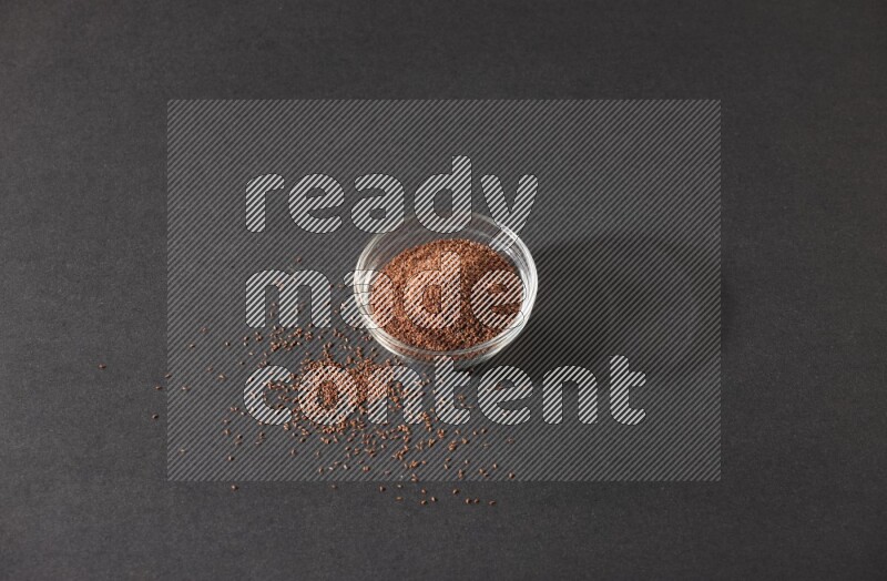 وعاء زجاجي ممتلئ ببذور حب الرشاد محاط بالبذور على أرضية سوداء