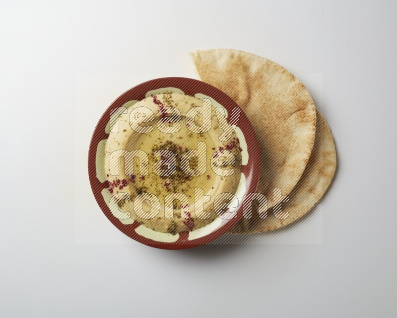 Hummus in a traditional plate garnished with zaatar & sumak on a white background