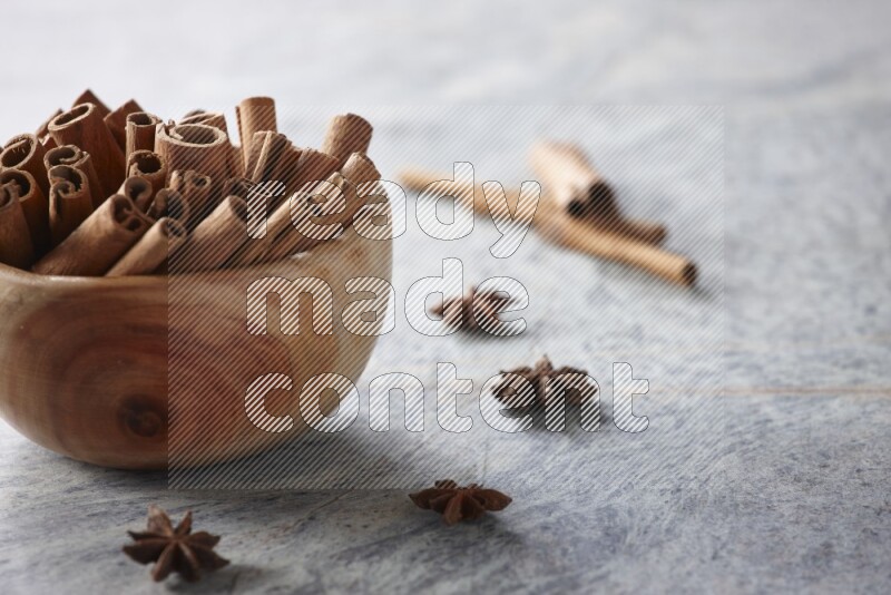 wooden bowl full of cinnamon sticks surrounded by star anis on marble background in different angles