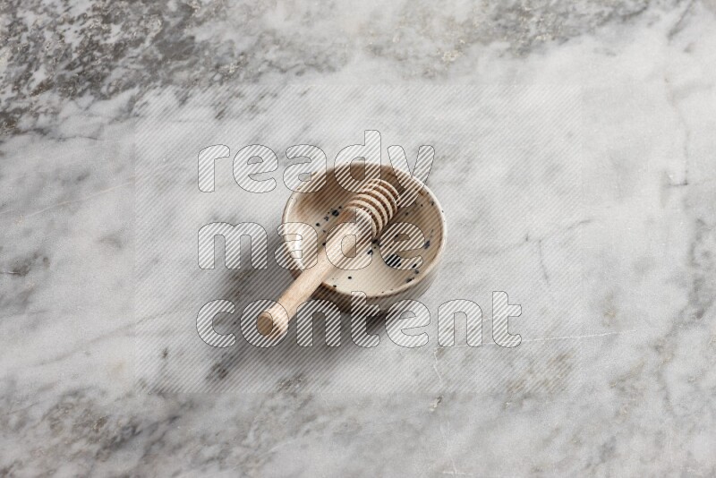 Multicolored pottery bowl with wooden honey dipper in it on grey marble background