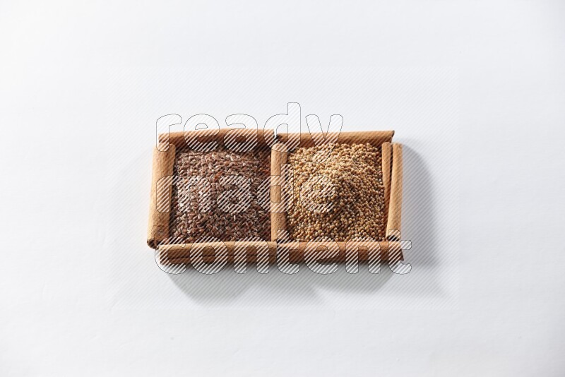 مربعان من أعواد القرفة ممتلئان بحبوب الخردل وبذور الكتان علي خلفية بيضاء