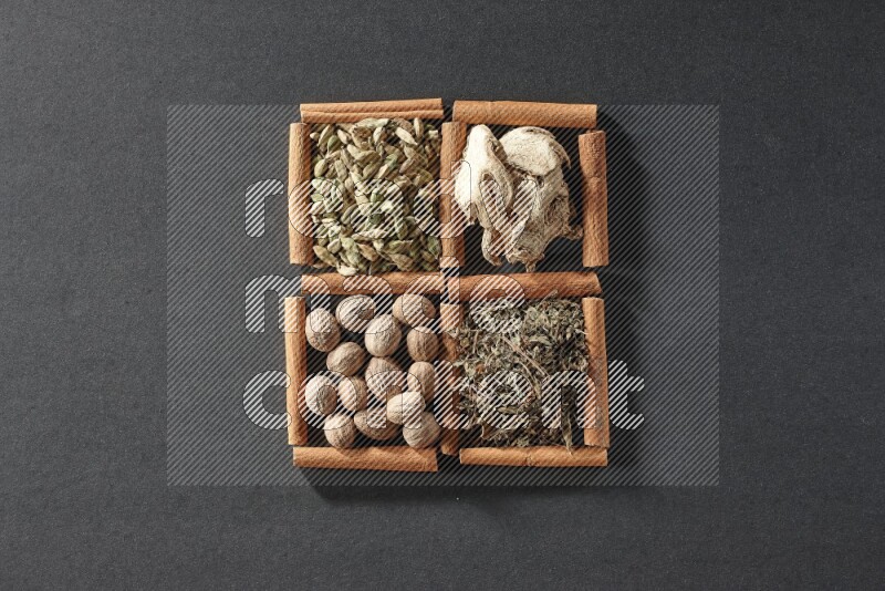 4 مربعات من عيدان القرفة ممتلئة بالريحان المجفف والهيل والزنجبيل المجفف وجوزة الطيب على أرضية سوداء