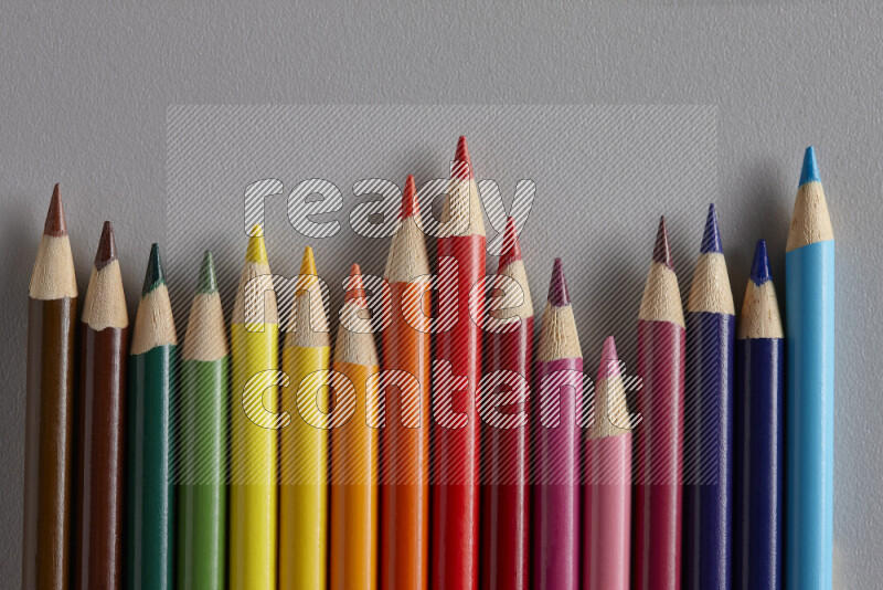 A collection of colored pencils arranged showcasing a gradient of different hues on grey background