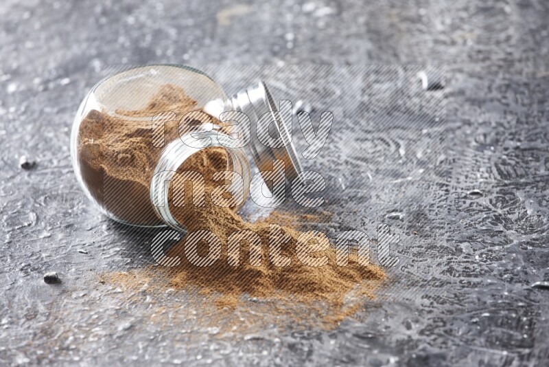 Flipped herbal glass jar full of cinnamon powder on textured black background