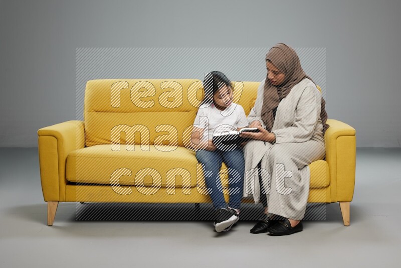 Mom and daughter sitting reading a book on gray background