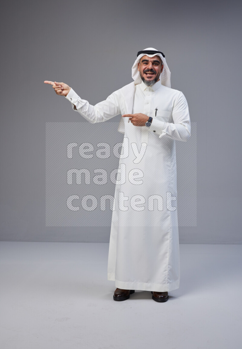 Saudi man Wearing Thob and white Shomag standing interacting with the camera on Gray background
