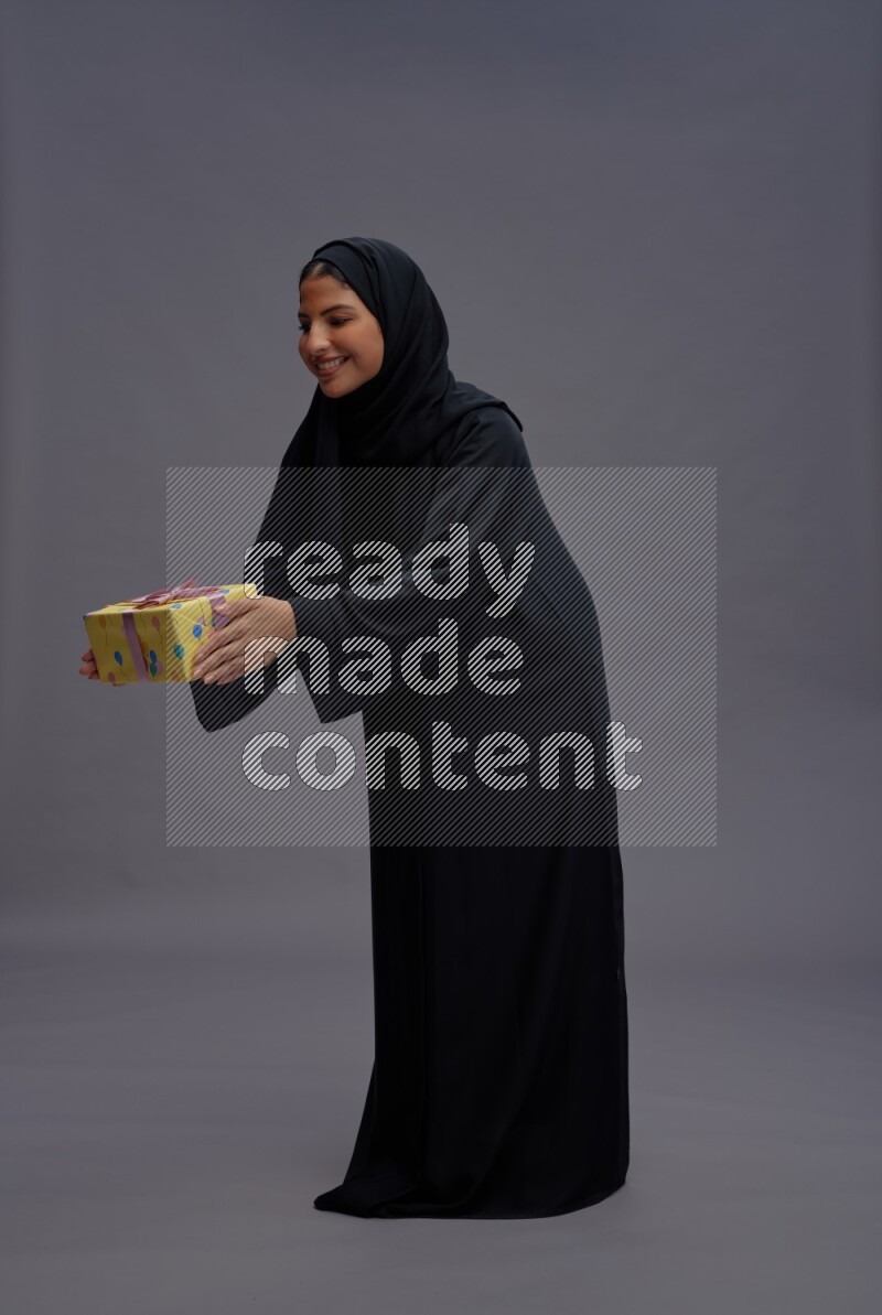 Saudi woman wearing Abaya standing holding gift box on gray background