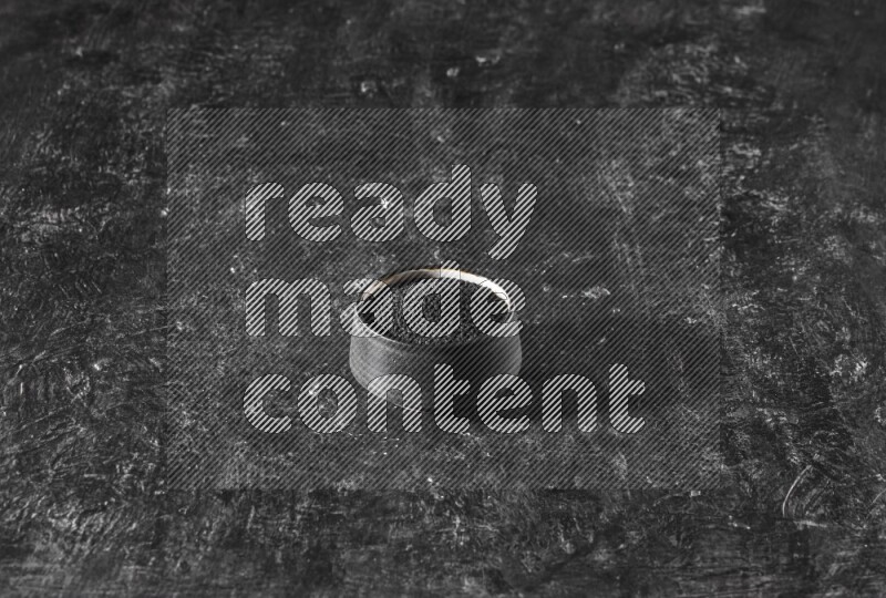 A black pottery bowl full of black seeds on a textured black flooring