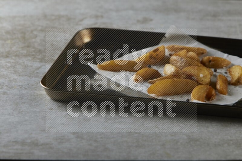 wedges potato on parchment paper in a black stainless steel rectangle tray on grey textured counter top
