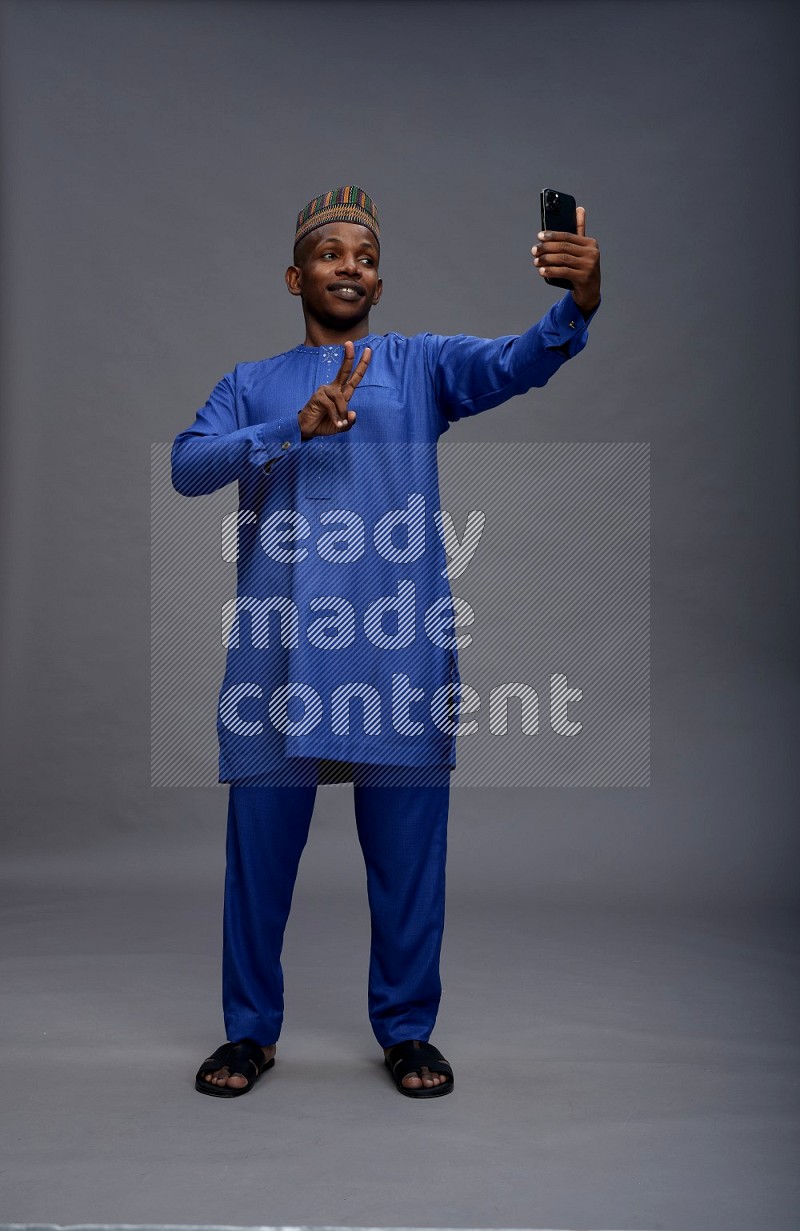 Man wearing Nigerian outfit standing taking selfie on gray background