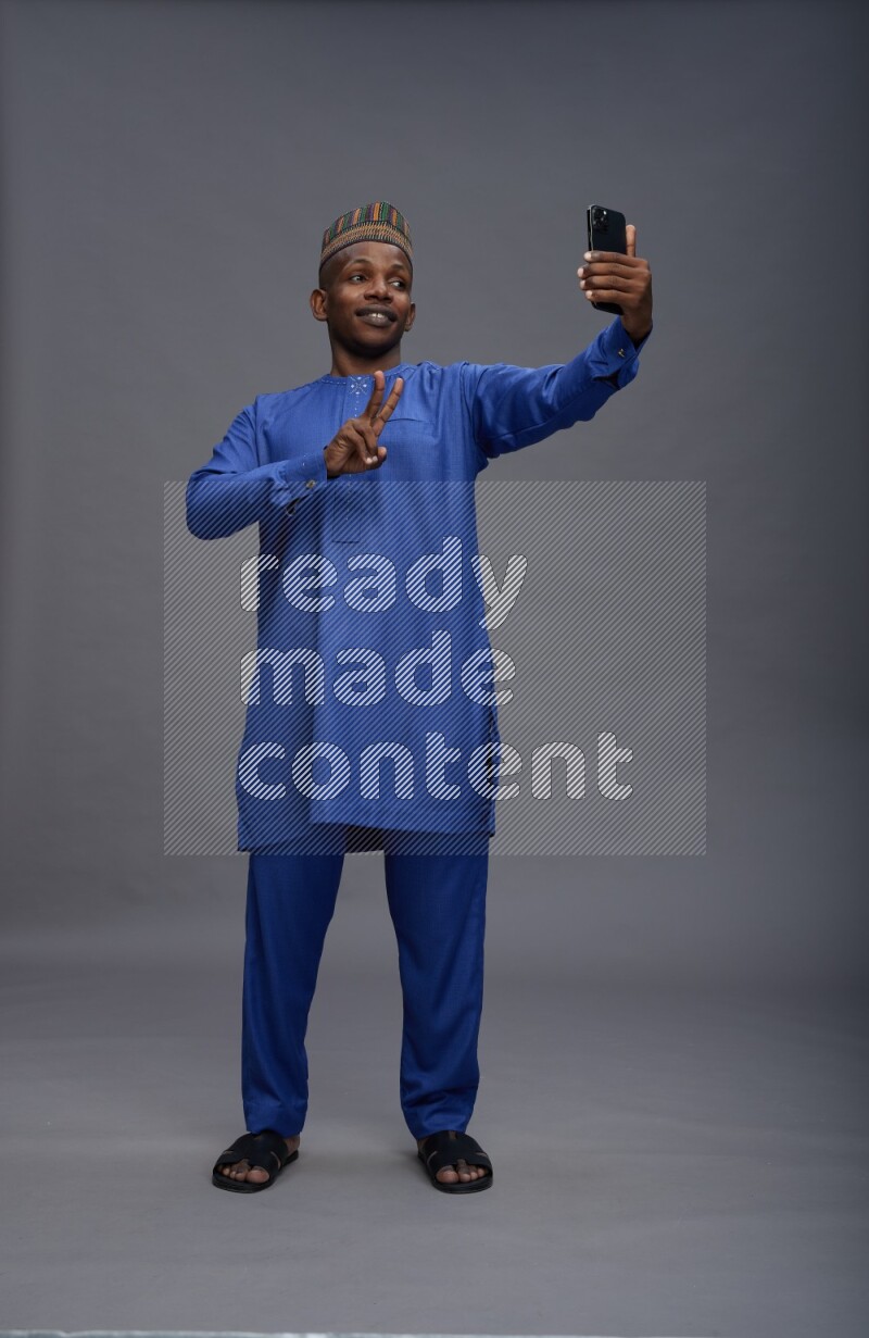 Man wearing Nigerian outfit standing taking selfie on gray background