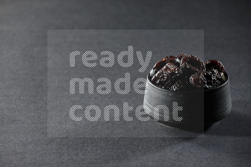 وعاء فخاري أسود ممتلئ بالبرقوق المجفف على خلفية سوداء