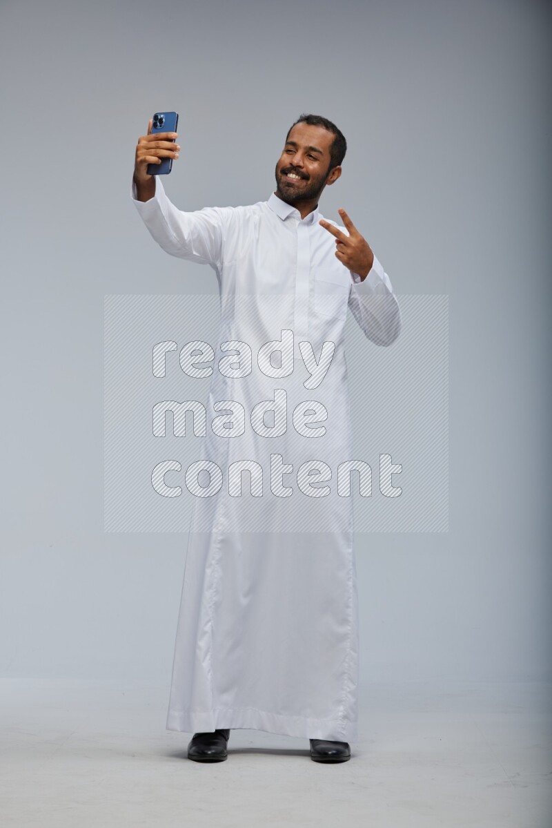 Saudi man wearing Thob standing taking selfie on Gray background