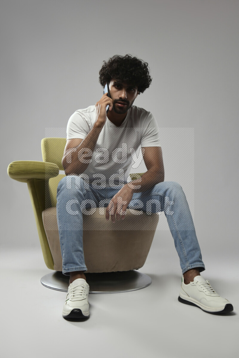 A man wearing casual sitting on a chair talking on the phone on white background