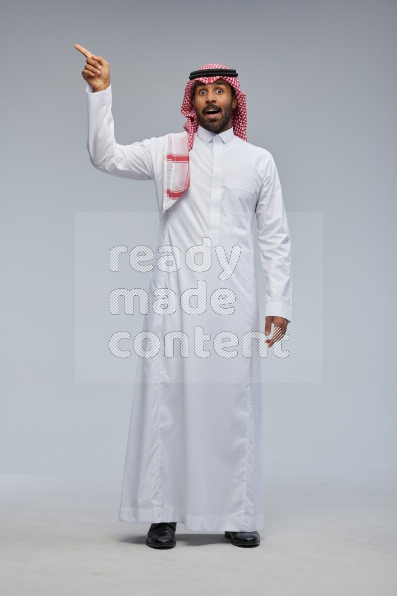 Saudi man Wearing Thob and shomag standing interacting with the camera on Gray background