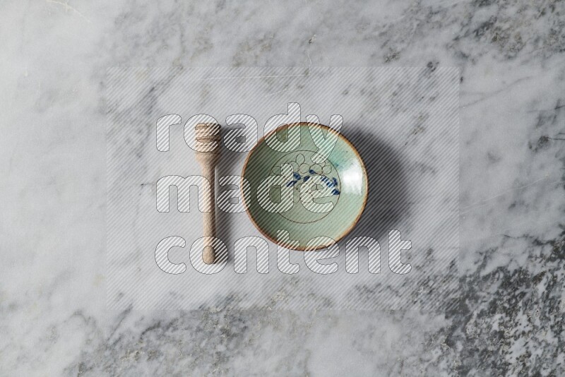 Decorative pottery plate with wooden honey dipper on the side on grey marble background