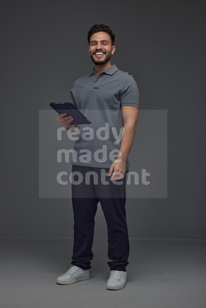 A man wearing casual standing and using his tablet and making multi hand gestures different angles eye level on a gray background