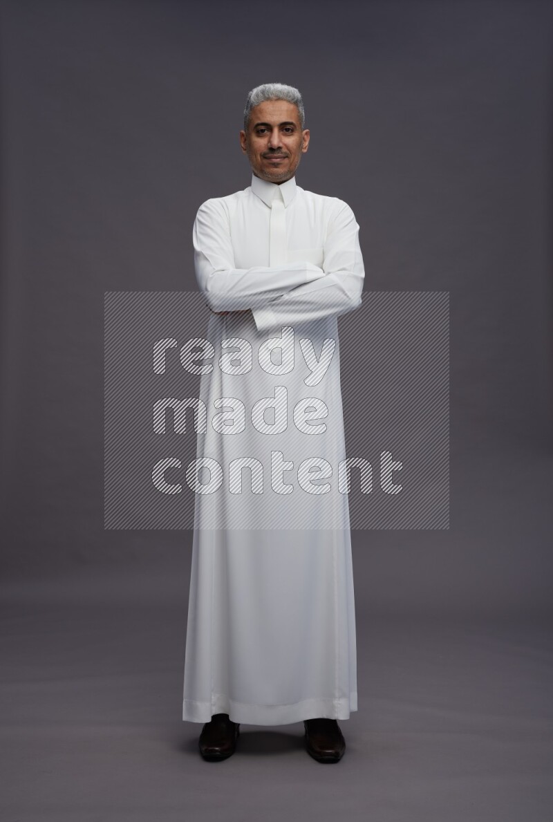 Saudi man wearing thob standing with crossed arms on gray background