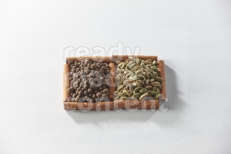 مربعان من أعواد القرفة ممتلئان بحبوب الهيل وحبوب الفلفل الحلو علي خلفية بيضاء