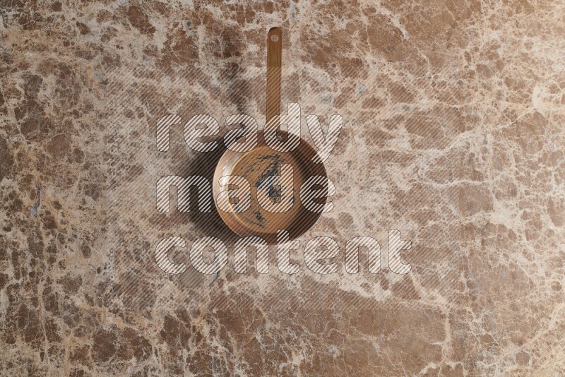A small copper pan on beige marble background