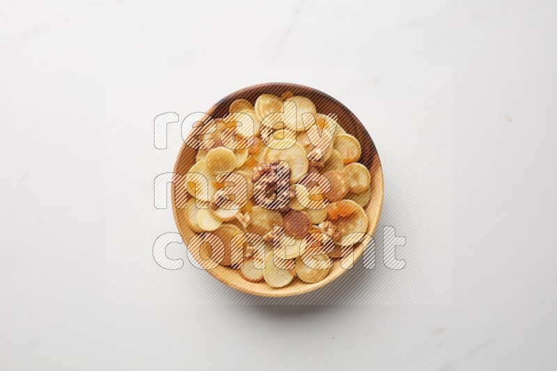 Top-view shot of walnut and apricot cereal pancakes in a round bowl on white background