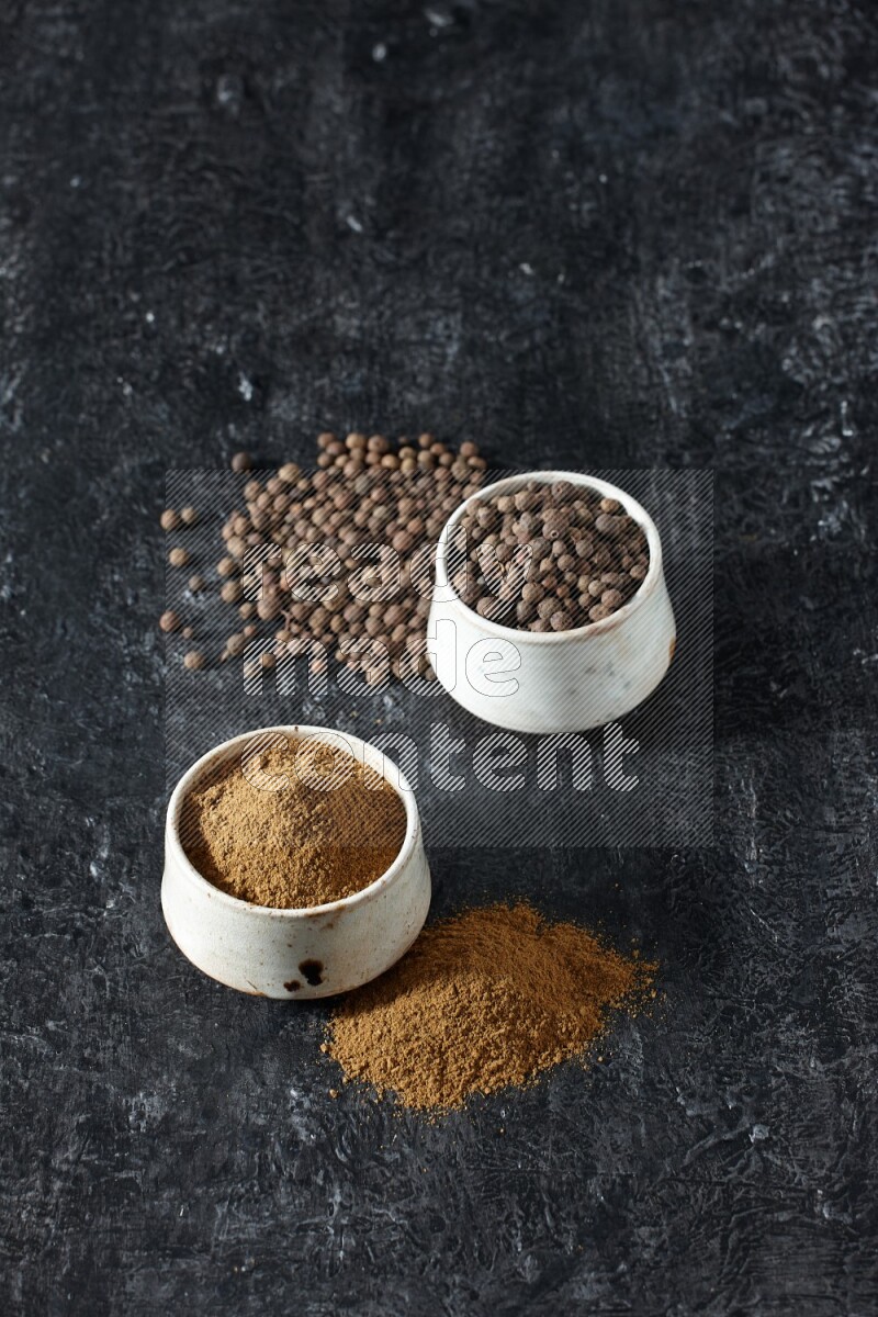 2 beige bowls, one full of allspice powder and the other full of whole balls and both spread on a textured black flooring