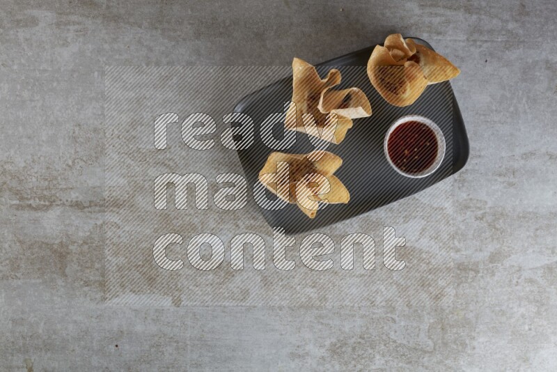wonton cups with soy sauce ramkin on rectangle dark grey ceramic plate on grey textured counter top