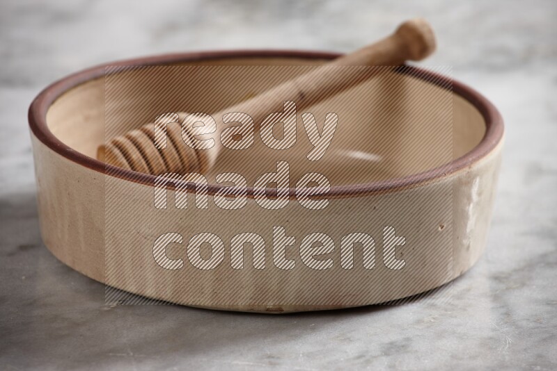 Beige Pottery Oven Bowl with wooden honey handle on the side with grey marble flooring, 15 degree angle